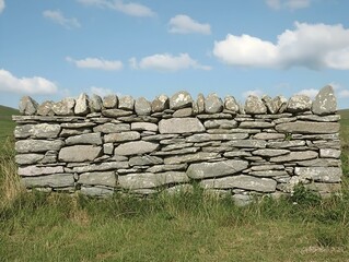 Rustic stone wall against a bright blue sky with fluffy white clouds. Ideal for backgrounds, textures, and rural themes.