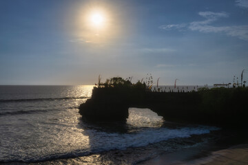Obraz premium Breathtaking sunset illuminating the ocean waves with a rocky arch silhouette, Pantai amed tabanan, capturing natures tranquility and beauty next to Tanah Lot Temple, Bali, Indonesia