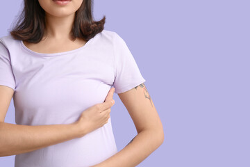 Young woman checking her breast on lilac background, closeup. Cancer awareness concept