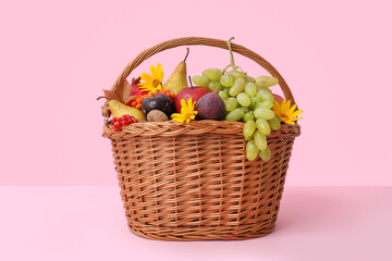 Wicker basket with different fresh fruits on pink background