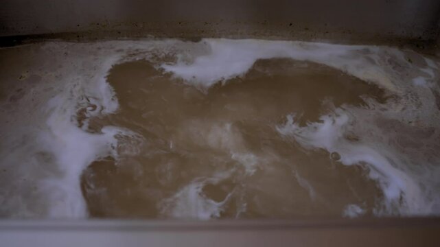 Stainless steel sink filled with the murky, brown water, a drainage issue, clogged pipes, or contaminated water supply. Dirty water is coming back to the sink.