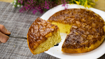 Homemade apple upside-down cake served on a white plate with floral decorations and a slice being served