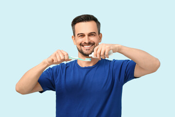 Fototapeta premium Handsome man squeezing tooth paste onto brush on blue background