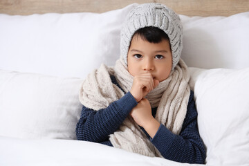 Ill little Asian boy coughing in bedroom