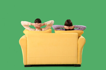 Beautiful young couple resting on sofa against green background, back view
