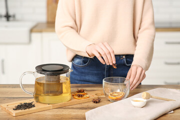 Young woman adding star anise in tea cup in kitchen