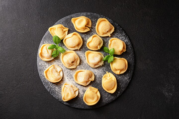 Board with raw dumplings and basil on black background