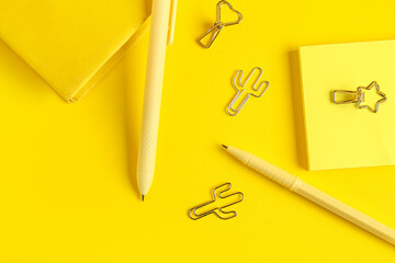 Pens with notebook, sticky notes and paper clips on yellow background