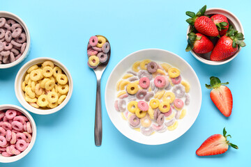 Bowls of colorful sweet cereal rings with milk and strawberries on blue background