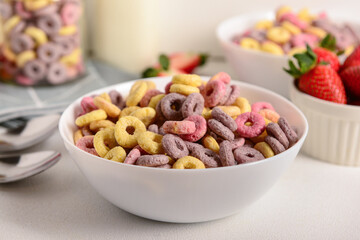 Bowls with colorful sweet cereal rings and strawberries on white table