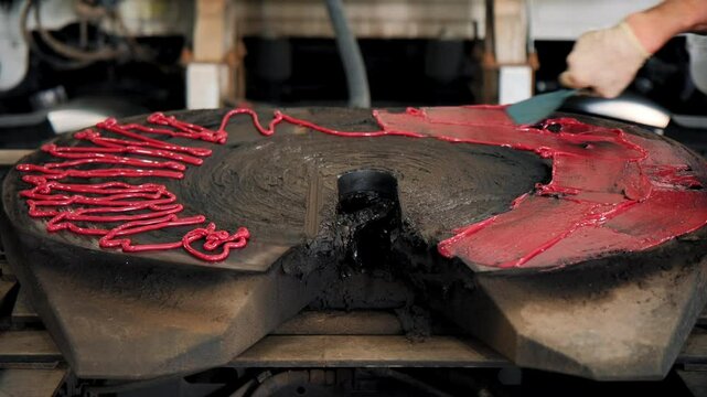 Mechanic covering the fifth wheel coupling on a truck with grease for lubrication, with red grease or marking compound applied around the edges. Truck is in repair shop during the inspection.