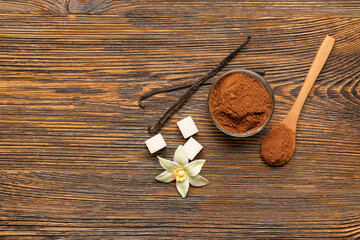 Bowl of cocoa powder, vanilla sticks, flower and sugar on wooden background