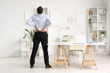 Young businessman suffering from lumbar pain in office, back view