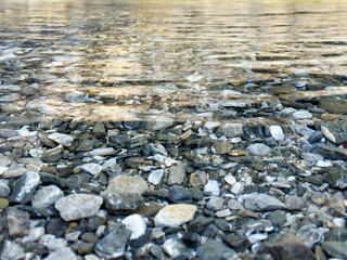 rippled river water with visible stones and smooth light reflections. soft wave patterns. clear mountain river water. calm and relaxing