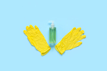 Rubber gloves with bottle of sanitizer on blue background