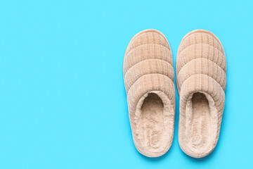 Pair of beige soft slippers on blue background. Top view