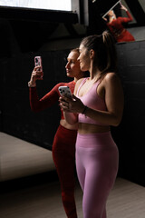 Two fitness girls taking selfie after workout session in gym's mirrored room