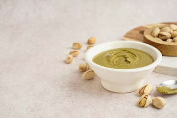 Bowl with tasty pistachio paste and spoon on pink grunge background