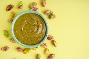 Bowl with tasty pistachio paste on yellow background