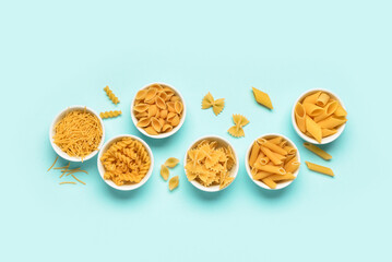 Bowls with different tasty uncooked pasta on blue background