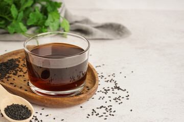 Glass of oil and wooden spoon with sesame seeds on white background