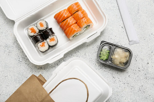 Plastic containers with tasty sushi rolls, marinated ginger and paper bag on blue grunge background. Delivery concept