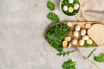 Wooden board with fresh boiled quail eggs, piece of bread and greens on light background