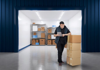 Man owner of storage unit. Guy is standing near warehouse gate. Man at entrance to storage unit. Businessman takes boxes from pantry. Persona with gadget rents storage room. Place for safekeeping