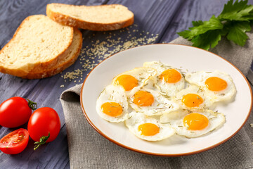 Plate with fried quail eggs, parsley and tomatoes on blue wooden background
