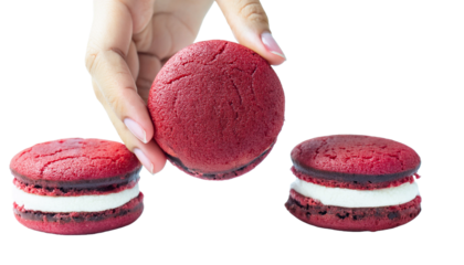 a person's hand holding a red velvet sandwich cookie, with two more cookies on the bottom
