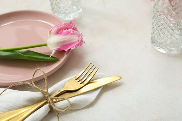 Beautiful table setting with pink plate, glass, cutlery, napkin and flower on light background, closeup