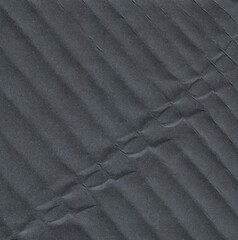Close-up of folded dark paper with small, repetitive wave-like ridges. The surface shows subtle...