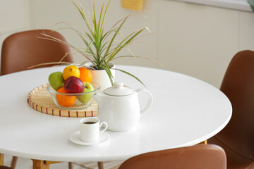Teapot with cup of coffee and fruits on dining table in kitchen, closeup