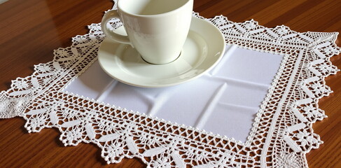 Elegant White Tablecloth with Lace Edging Under a White Coffee Cup and Saucer on Wooden Table