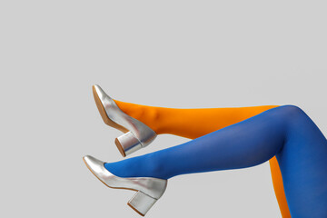 Legs of young woman in colorful tights and silver shoes on white background