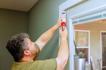 Carpenter uses caulking gun to seal gaps around doorframe, enhancing room interior during...