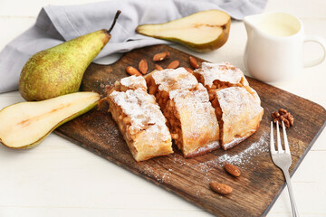 Wooden board with pieces of tasty pear strudel and fresh fruits on light background