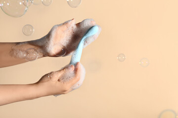 Woman washing vibrator and soap bubbles on beige background, closeup