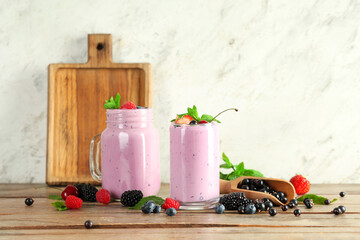 Glass and mason jar of fresh smoothie with different berries on wooden table