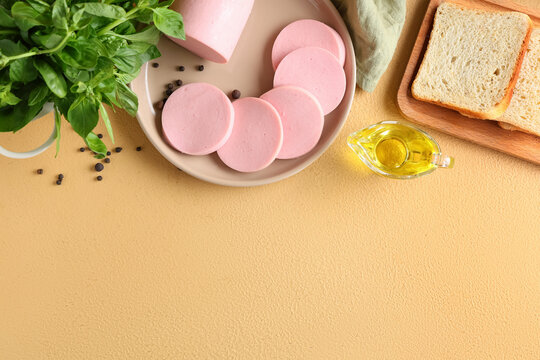 Plate with slices of tasty boiled sausage, bread and basil on beige background