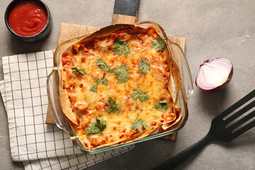 Baking dish with tasty enchilada and tomato sauce on grunge background