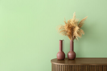 Vase with dry reeds on dresser near green wall in living room