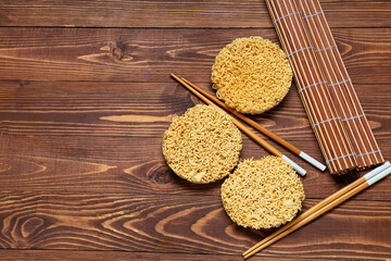 Raw instant noodles with chopsticks and bamboo mat on wooden background