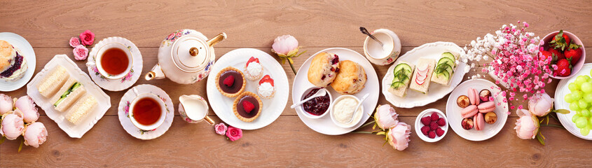 Afternoon tea table scene against a light brown wood banner background. Vintage tea set, finger...