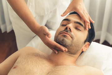 Caucasian man enjoying relaxing anti-stress head massage and pampering facial beauty skin recreation leisure in dayspa modern light ambient at luxury resort or hotel spa salon. Quiescent