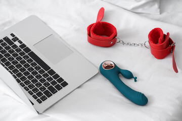 Vibrator with handcuffs and laptop on bed, closeup