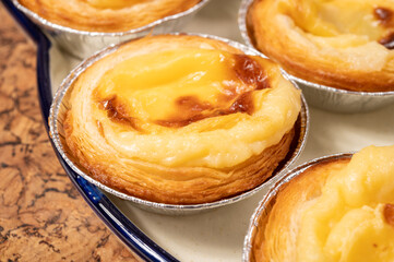 Portugal's traditional sweet dessert Pastel de nata egg custard tart pastry in cup close up on wooden background