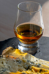 Whiskey and cheese pairing, tasting whisky glass and plate with sliced blue stilton and blue...
