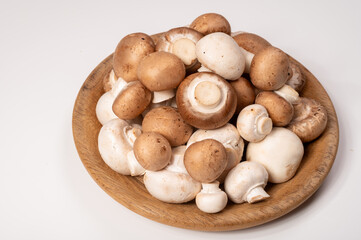 White and brown champignons mushrooms fresh uncooked on wooden plate copy space on white background