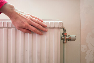 Checking the warmth of a white cast iron radiator. A hand in a red sleeve touches the heating unit...